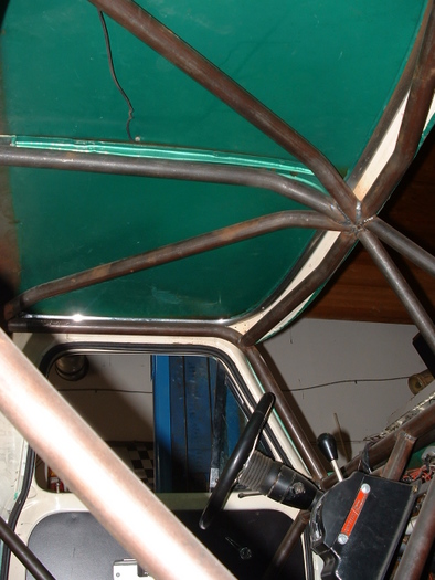 1977 Ford F-150 - The interior of a vehicle is visible, a roll cage structure and a green headliner, with a steering wheel and gear shifter present.
