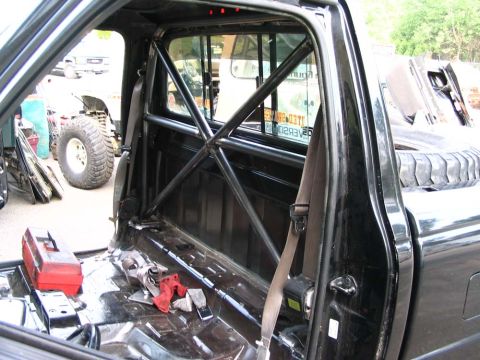 1977 Ford F-150 - Pickup truck interior modified with a roll cage, with another vehicle visible outside.