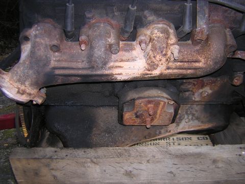 1979 Ford Bronco - Close-up of a corroded engine part, resting on wooden planks, with some text visible on a box beneath.