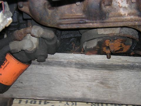 1979 Ford Bronco - Close-up view of an engine mount and an orange oil filter resting on wooden planks.