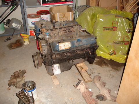 1979 Ford F-150 - A V8 engine sits on wooden blocks in a garage, surrounded by various automotive parts and storage items.