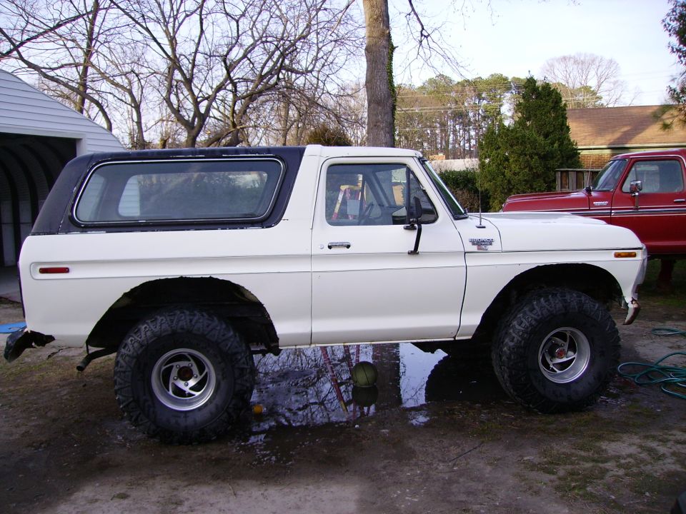 White 1979 Ford Bronco with black top parked next to a red pickup truck