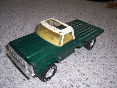 1978 Ford Bronco - A green toy truck with a white roof and yellow windows sits on a carpeted surface.