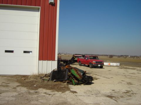1992 Ford Bronco - A red 1992 Ford Bronco is parked with a trailer next to a large building, with scrap metal in the foreground.