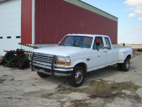 1992 Ford Bronco - This white Ford F-350 dually pickup truck is parked outside a large red barn with farm equipment nearby.