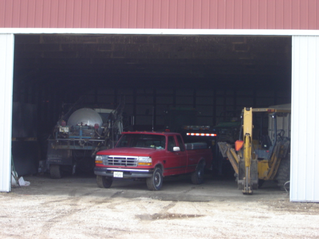 Red 1992 Ford F-150 pickup truck parked inside a barn with farm equipment
