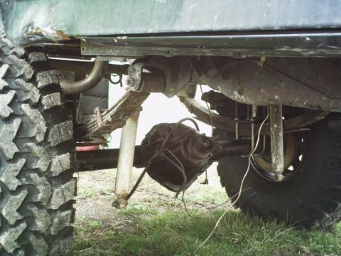 1986 Ford Bronco - Close-up view of the rear axle, leaf springs, and shock absorber assembly on a vehicle with aggressive off-road tires.