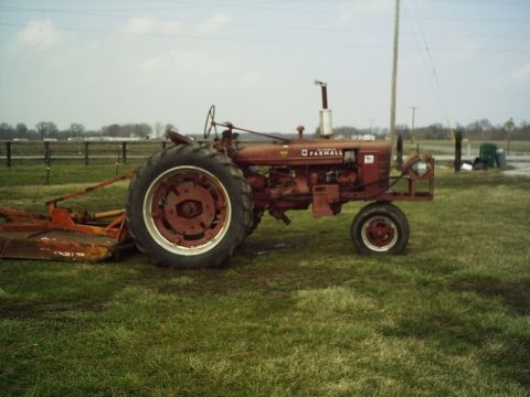 1986 Ford Bronco - A red Farmall tractor with a mower attachment sits in a field under an overcast sky.
