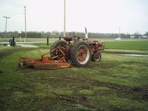 1986 Ford Bronco - A red tractor with an attached mower sits in a grassy, muddy field under an overcast sky.