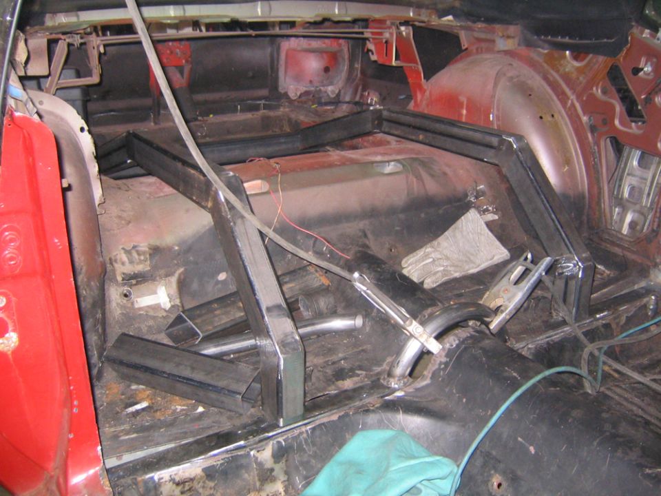 car interior being modified with metal bars for a roll cage, welding equipment visible