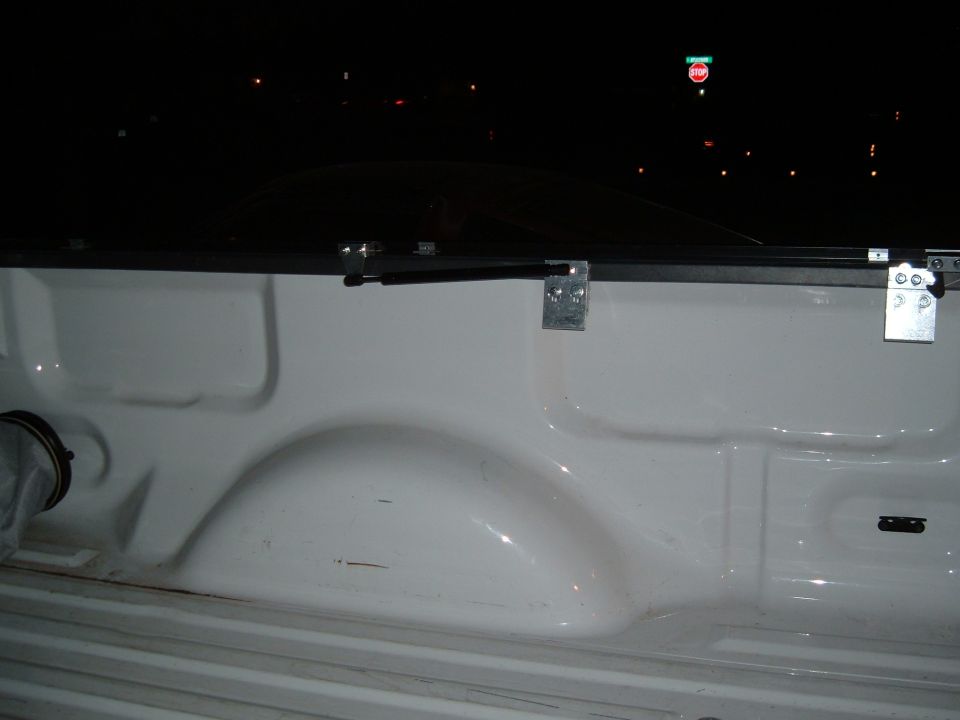 White truck bed with visible wheel well and mounting hardware for a tonneau cover. A "SUPERMOTORS" watermark is present