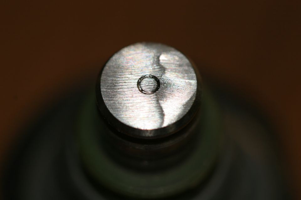 Close-up of a metal fuel injector top with a small circular opening