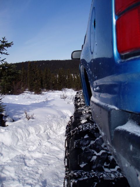 2000 Ford E350 - A blue van equipped with snow chains navigates a snowy terrain.