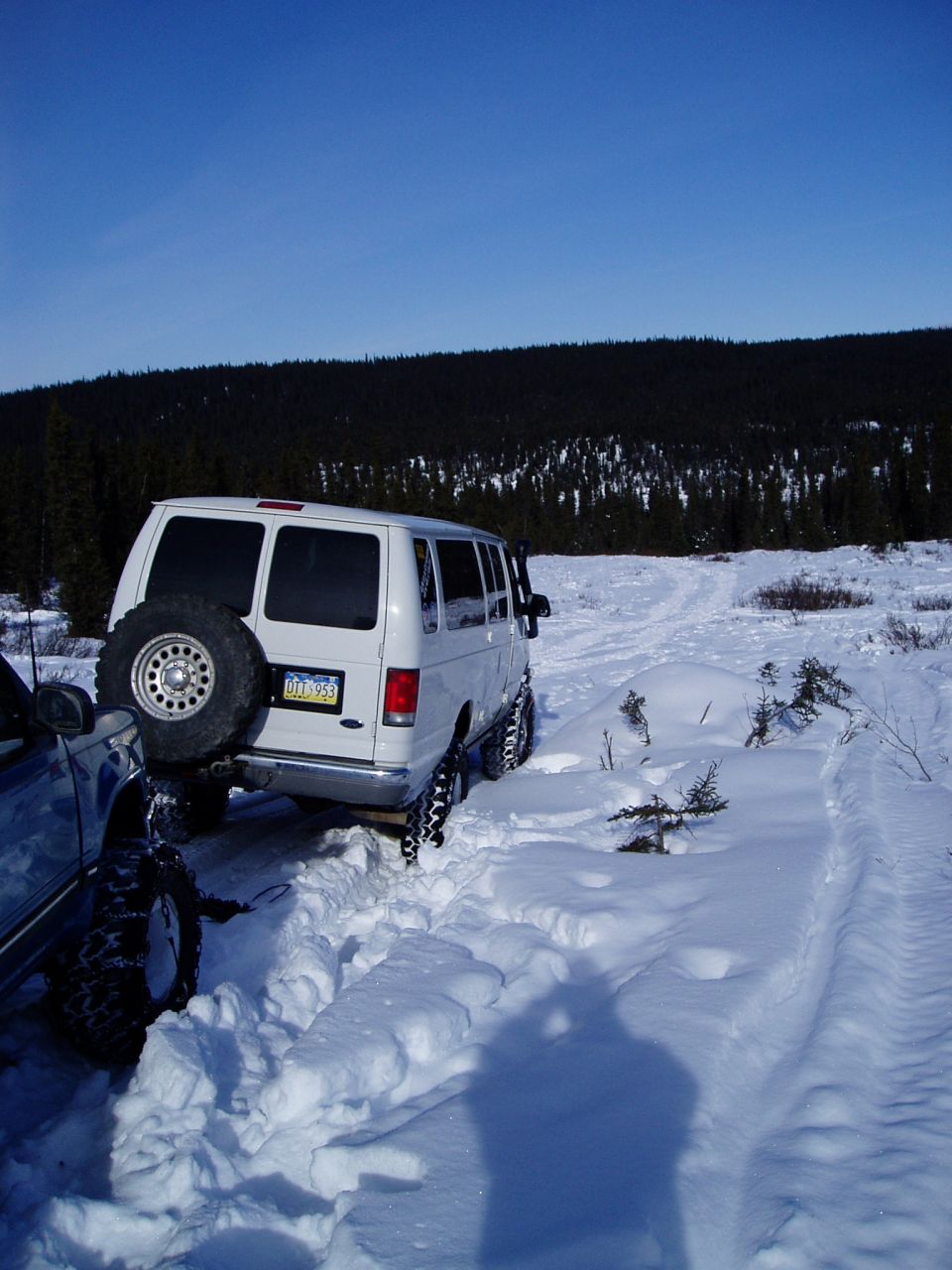 White Ford E350 van with spare tire on back stuck in deep snow next to another vehicle