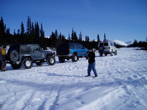 2000 Ford E350 - Several off-road vehicles are parked in a snowy, wooded area under a clear blue sky.