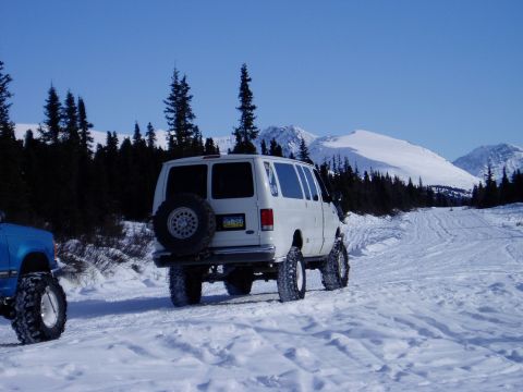2000 Ford E350 - A white van with a spare tire mounted on the rear is seen driving in a snowy, mountainous area.