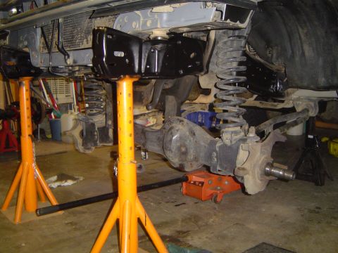 1989 Ford Bronco - The vehicle's undercarriage is supported by jack stands, revealing its suspension and differential components.