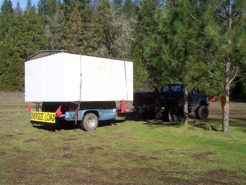 1994 Ford F-150 - A black pickup truck tows a trailer carrying a large, white, modular structure, marked as an oversized load.