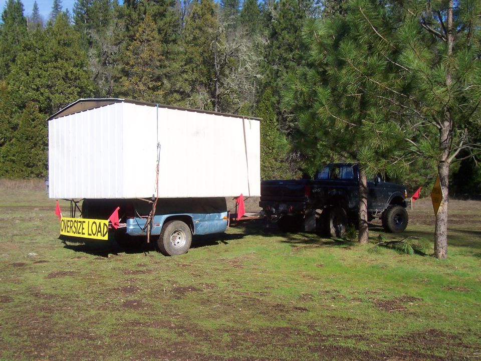 Black pickup truck towing an oversized load trailer in a grassy area