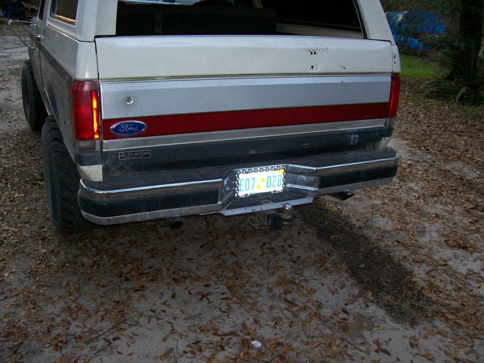 Rear of white and silver Ford SUV with Florida plate on chrome bumper, parked on dirt