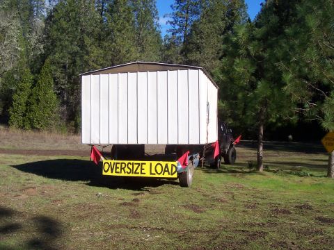 1994 Ford F-150 - A trailer carries a shed, marked as an oversize load, in an outdoor setting.