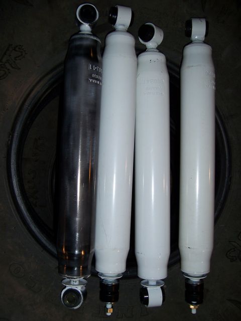 1983 Ford Bronco - Four shock absorbers are displayed, with one in dark metal and three in white, resting on a tire.