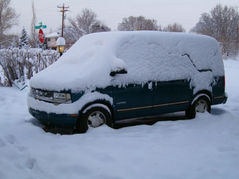 1985 Ford Bronco - A teal van is partially buried in snow on a winter day.