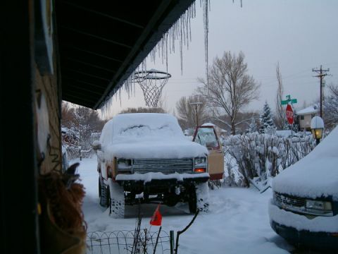 1985 Ford Bronco - Two SUVs, including a 1985 Ford Bronco, are parked and covered in snow.