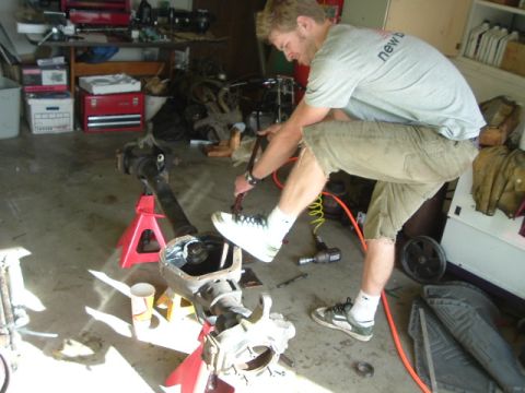 1989 Ford Bronco - A man works on a vehicle's axle assembly, which is supported by red jack stands in a cluttered garage.