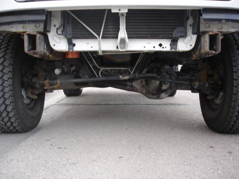 1996 Ford Bronco - Undercarriage view of a white vehicle's front axle and suspension system.
