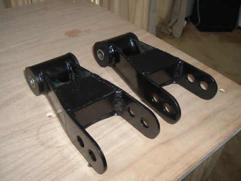 1989 Ford Bronco - Two black metal suspension lift blocks with bushings and mounting holes are displayed on a wooden surface.