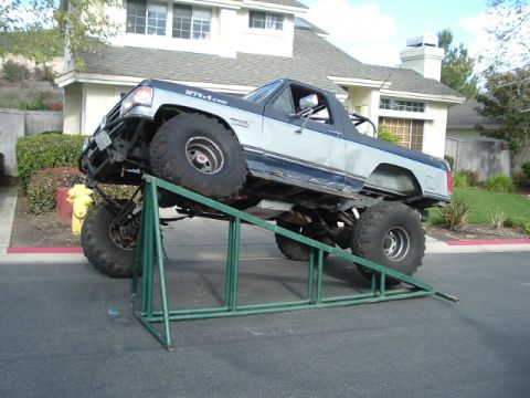 1989 Ford Bronco - Modified 1989 Ford Bronco with lifted suspension and large tires is positioned on a green metal ramp.
