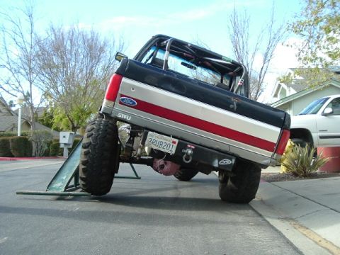 1989 Ford Bronco - Modified Ford Bronco with off-road tires is positioned on a ramp, with another vehicle visible in the background.