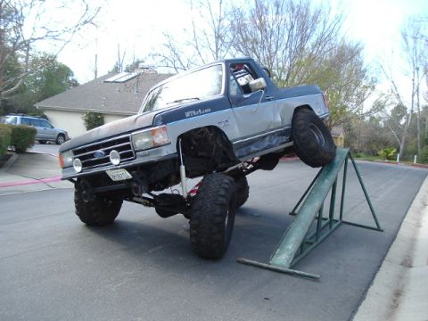 1989 Ford Bronco - This heavily modified SUV, likely a 1987 model, is shown on a ramp, demonstrating its off-road capabilities.