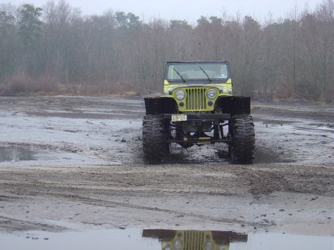 1987 Suzuki Samurai - A lifted Jeep CJ-5 navigates a muddy terrain, its large tires kicking up dirt.