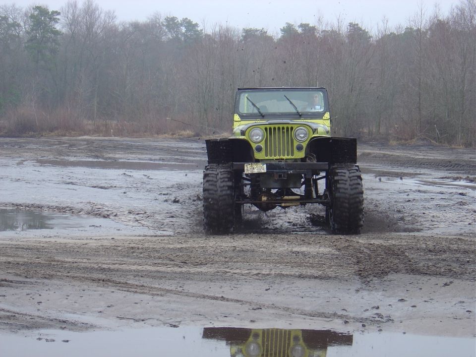 Yellow Jeep CJ-5 with large tires driving through mud, front view