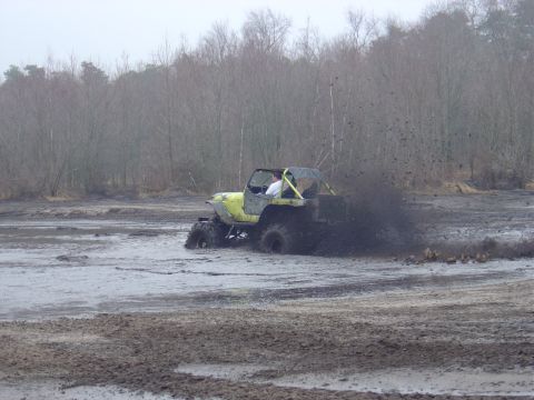 1987 Suzuki Samurai - A yellow off-road vehicle navigates a muddy track, sending mud flying.
