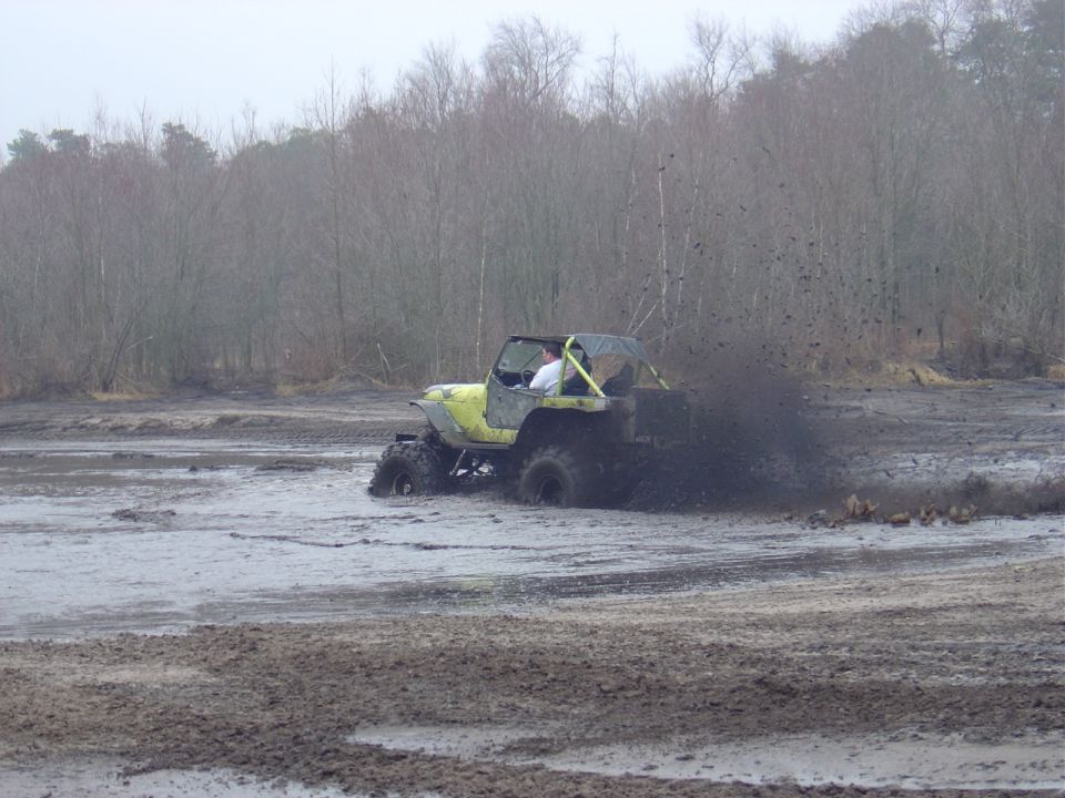 Yellow off-road vehicle kicking up mud, side view