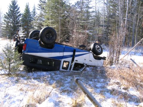 1985 Ford Bronco II - A blue and white 1985 Ford Bronco II lies on its side in a snowy, wooded environment after an apparent accident.