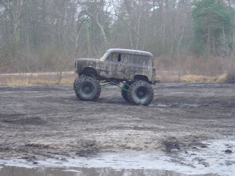 Mud-covered custom off-road vehicle with oversized tires and suspension lift, driving through a muddy field