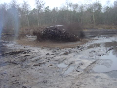 1987 Suzuki Samurai - A vehicle navigates a muddy terrain, kicking up a large spray of mud.