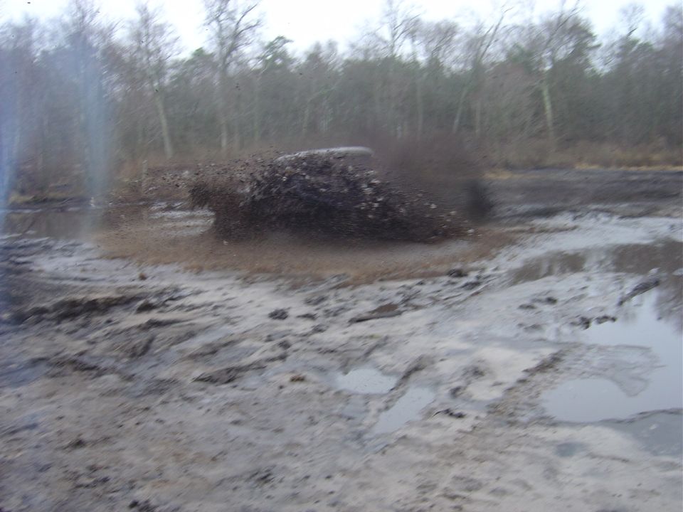 off-roading vehicle splashing through mud, trees in background