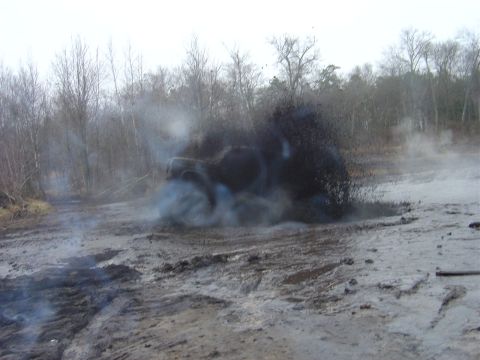 1987 Suzuki Samurai - An off-road vehicle navigates a challenging muddy track, kicking up dirt and smoke.