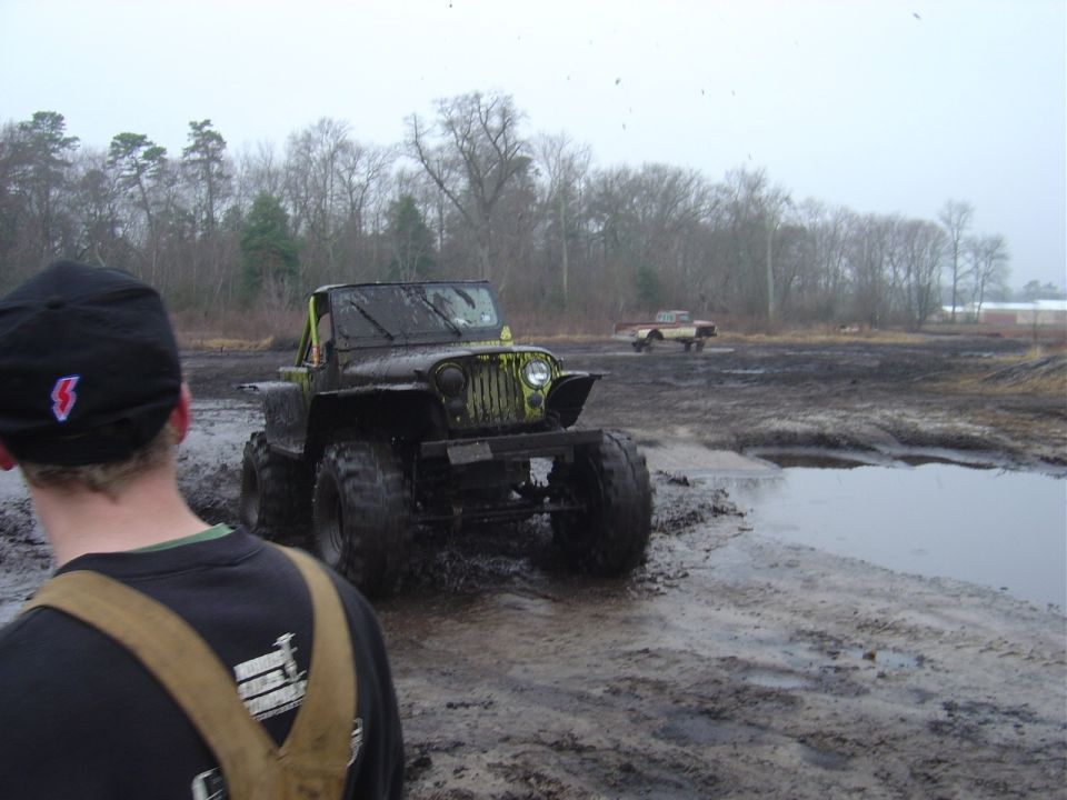 Modified Jeep with large tires driving through mud, another truck in background