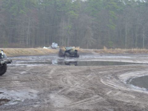 1987 Suzuki Samurai - Off-road vehicles are seen driving through a muddy area with trees in the background.