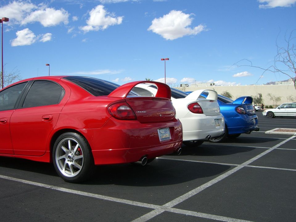 Red Dodge Neon SRT-4 rear view with spoiler, parked in a lot with white and blue Neon SRT-4s