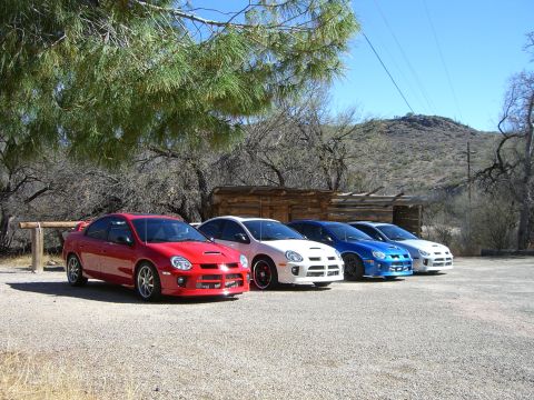1996 Ford Probe - A lineup of four Dodge Neon SRT-4s are parked in a gravel lot with a rustic building and desert landscape in the background.