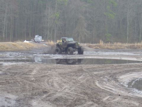 1987 Suzuki Samurai - Off-road vehicle navigating a muddy terrain with trees in the background.