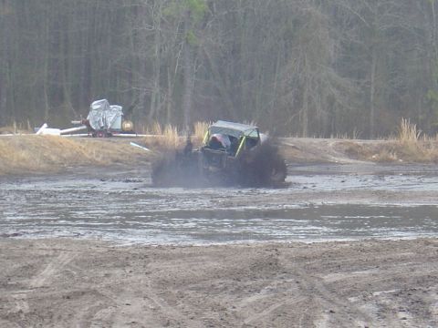 1987 Suzuki Samurai - An off-road vehicle navigates a muddy terrain, kicking up a large spray of mud.