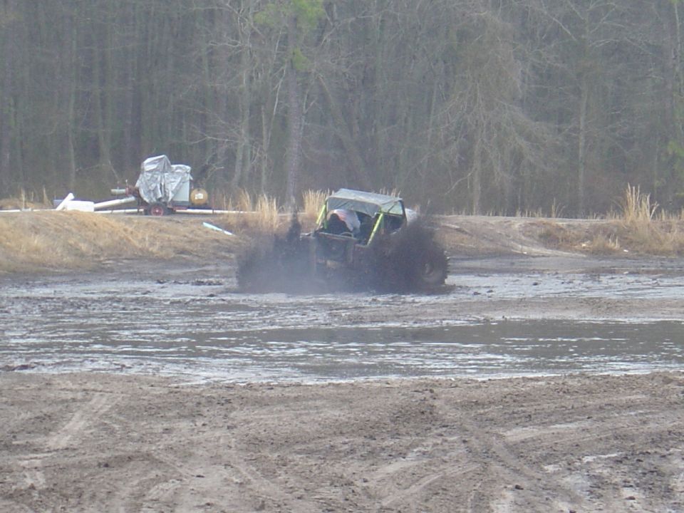 Off-road vehicle splashing mud while driving through a muddy field